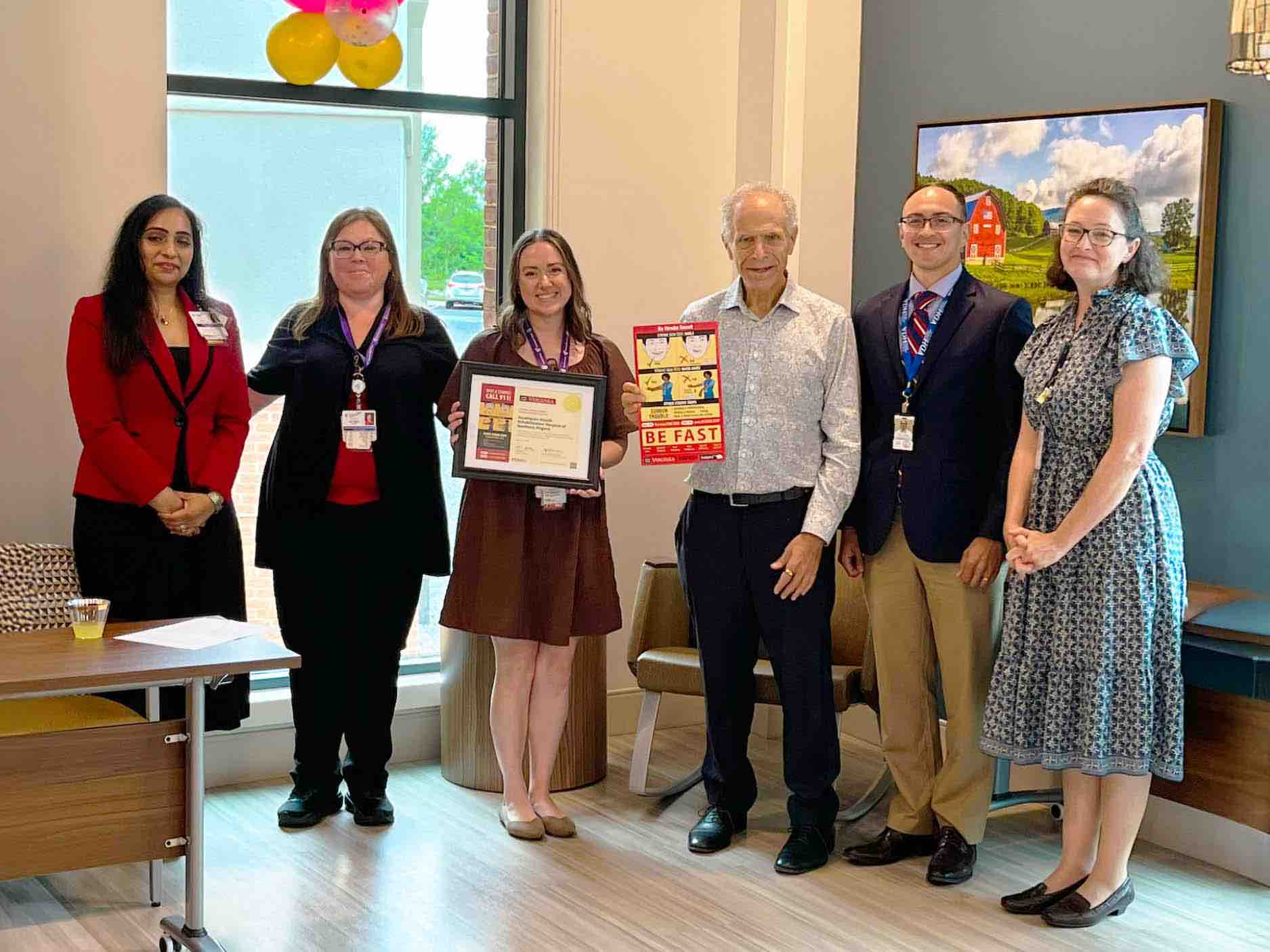 Rehabilitation hospital team and community members present Stroke Smart education, holding certificate and BE FAST stroke awareness poster during prevention outreach event in clinic setting