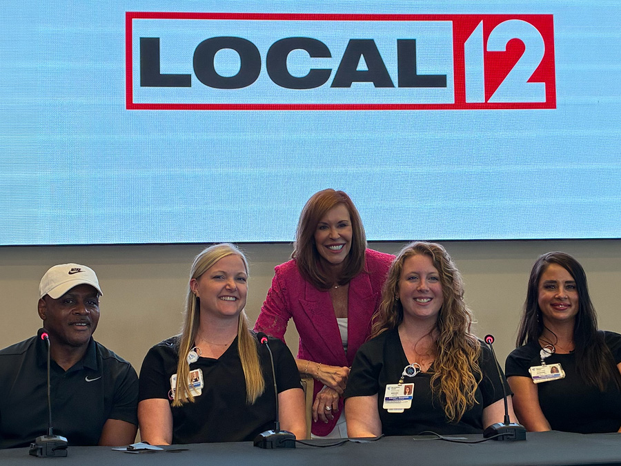 Panel participants and a presenter pose beneath a Local 12 display during a community event.