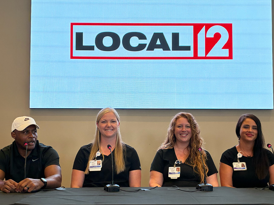Panel participants pose beneath a Local 12 display during a community event.