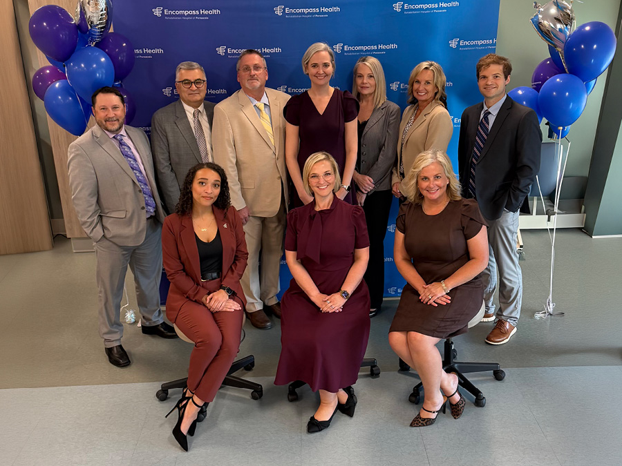 Leadership team members pose for a group photo in front of an Encompass Health backdrop with blue and silver balloon decorations.