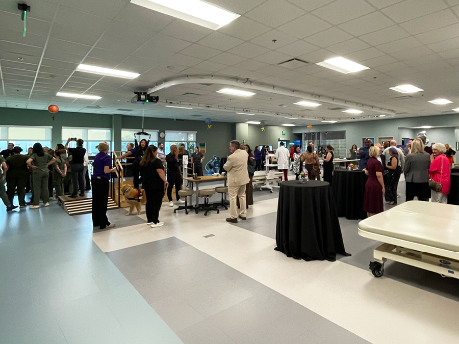 Guests attend an open house in a rehabilitation therapy gym, mingling among therapy equipment and treatment areas.