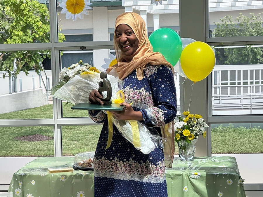 Daisy Award recipient Zenab Kone holds flowers and a recognition award during a daisy-themed healthcare appreciation ceremony.