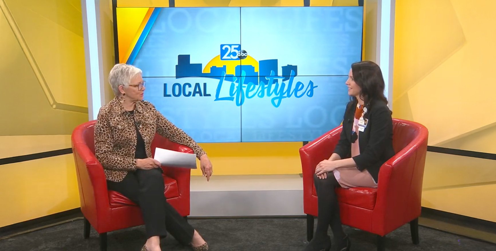 A rehabilitation specialist seated in a studio chair during a televised segment discusses Parkinson’s Disease awareness and therapy resources, with a bright backdrop and program logo visible.