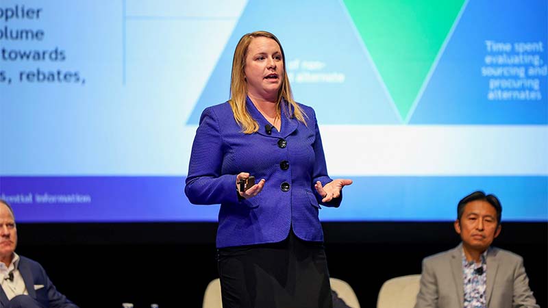 Elaine Prince presents during a professional conference, standing on stage with supporting panelists as presentation slides display behind her, highlighting leadership strategy.
