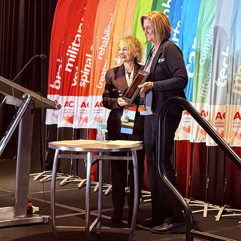 Award recipient Cheryl Miller accepts a plaque during an American Congress of Rehabilitation Medicine conference presentation on stage.