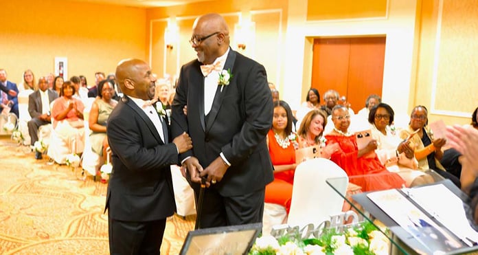 Jeff, a stroke survivor, walks down the aisle at his wedding with a loved one at his side, surrounded by guests seated in a warmly lit ceremony room.