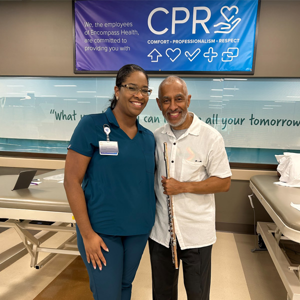 Nestor Torres with his flute posing with an Encompass Health case manager