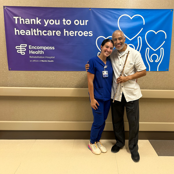 Grammy award winner,Nestor Torres, posing with an Encompass Health occupational therapist while holding his flute