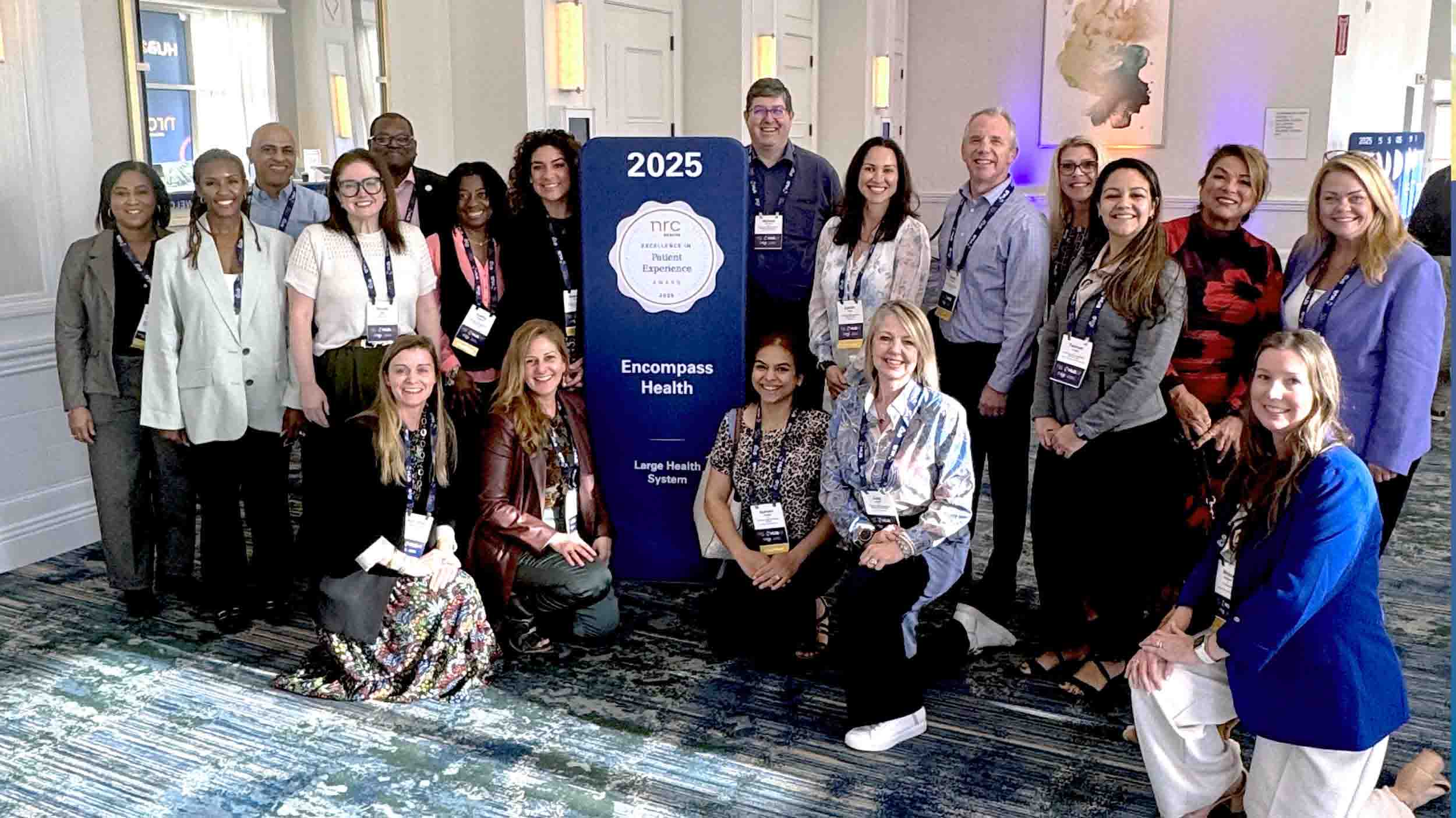 A diverse group of 19 people smiles around a sign reading 