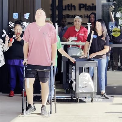 Officer James Black walking out of Encompass Health South Plains on a walker with nurses and staff cheering