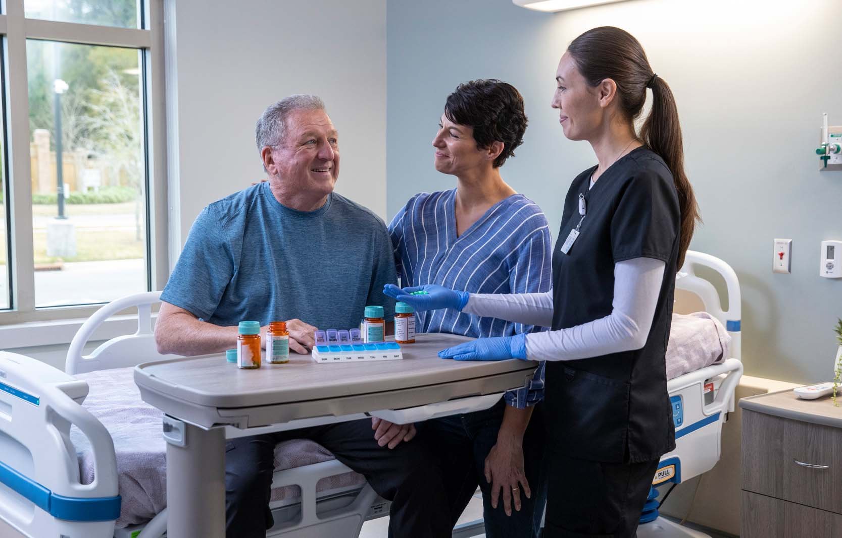 A healthcare professional reviews medications with a patient and visitor during hospital discharge planning.