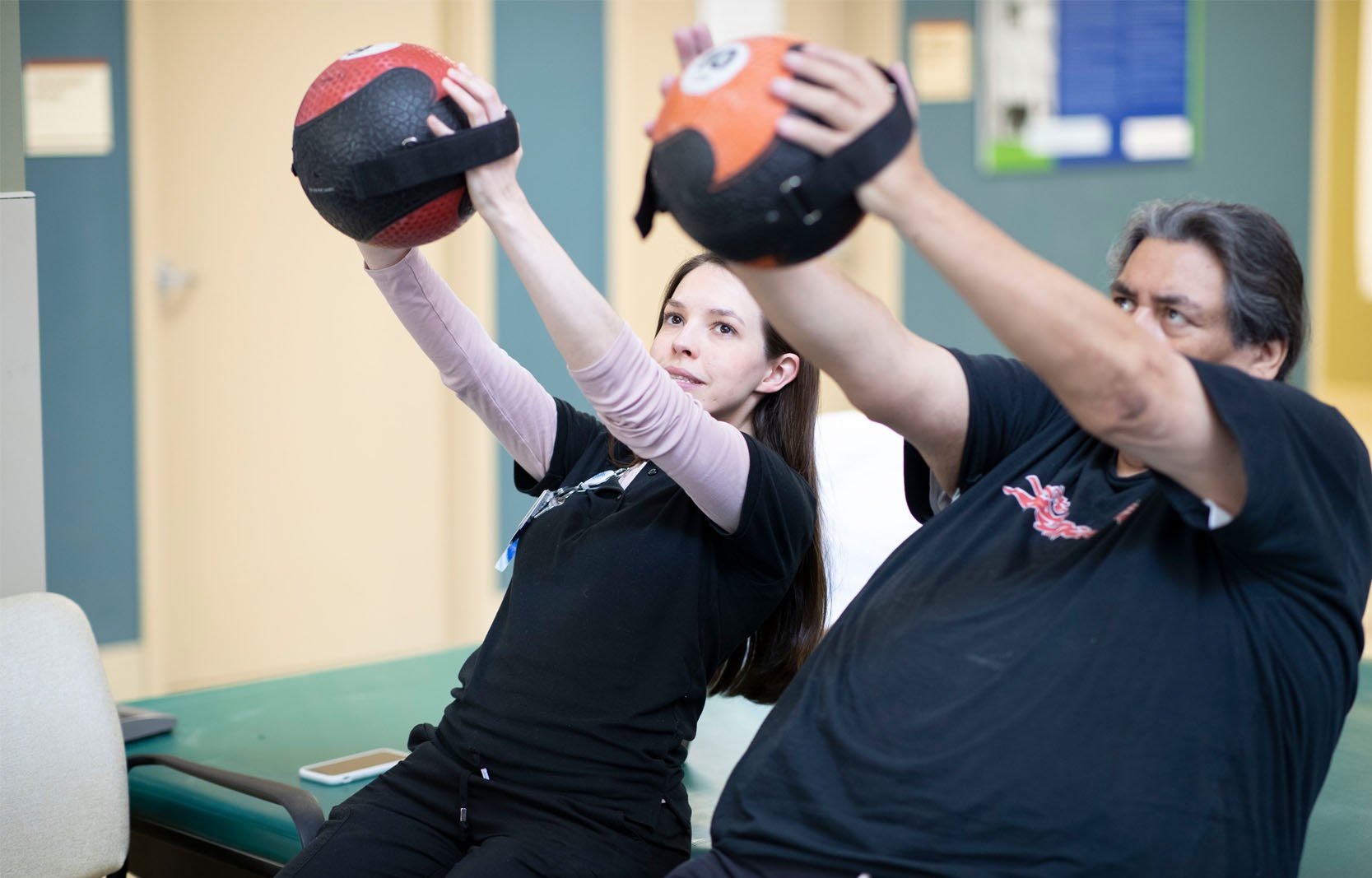 A therapist and patient perform a seated medicine ball exercise during a rehabilitation therapy session.