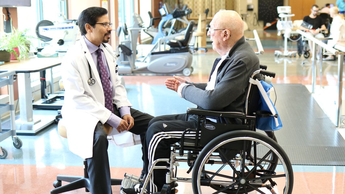 A physician speaking with a patient in a wheelchair
