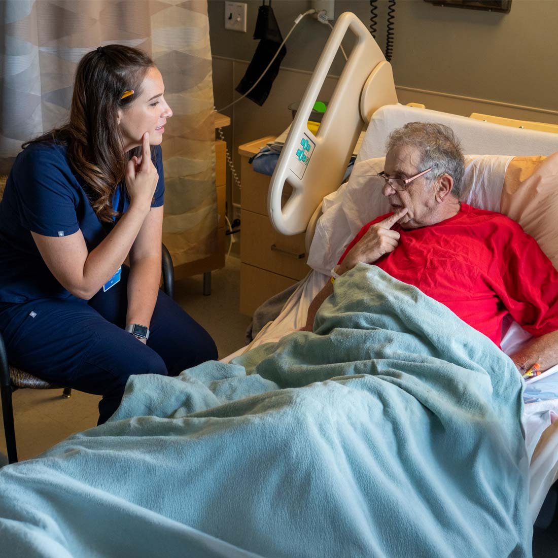 A speech therapist meeting with a patient at his bedside
