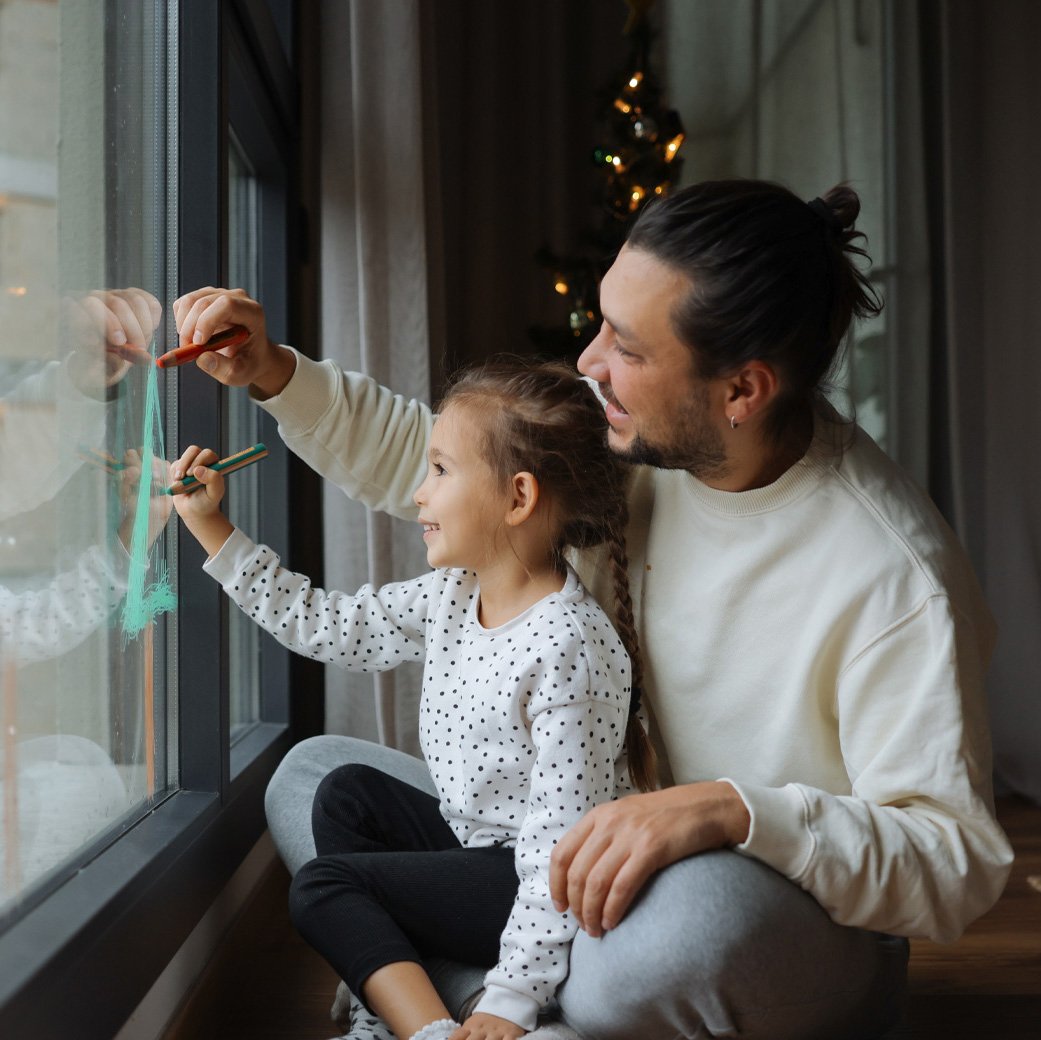parent and child sitting on the floor painting the window