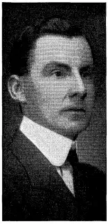 A black and white portrait of a man with dark hair, wearing a suit and tie, looking slightly to the right.