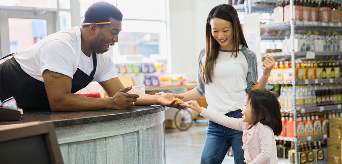 Woman and her young daughter chat with a clerk behind the counter at a small business.