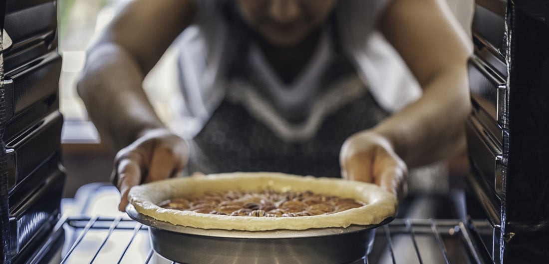 woman places pecan pie in oven