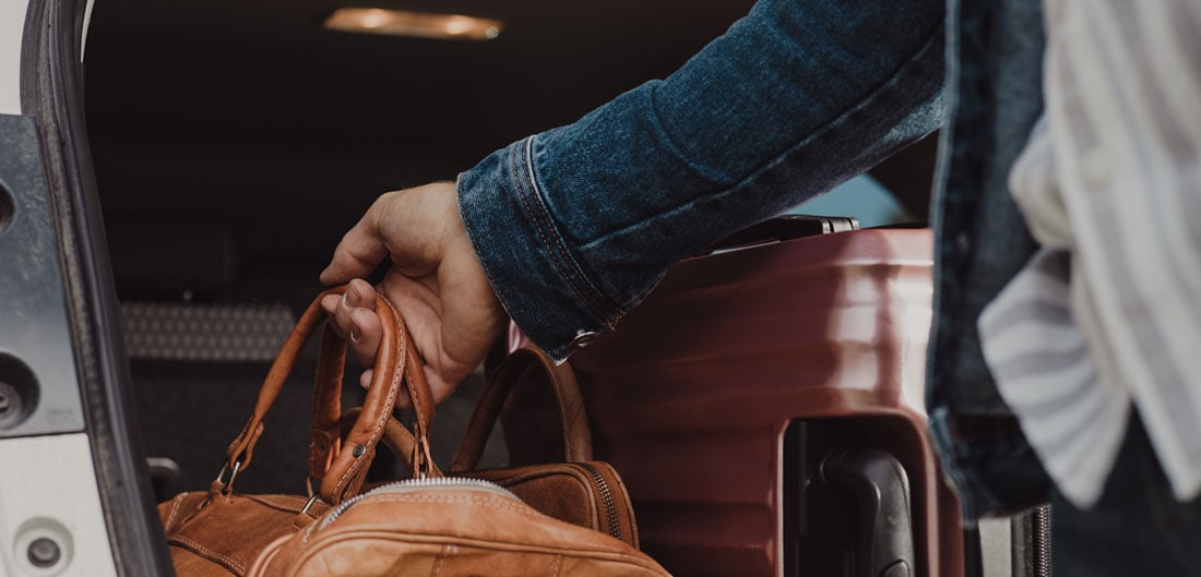 hand grabs leather suitcase from back of car