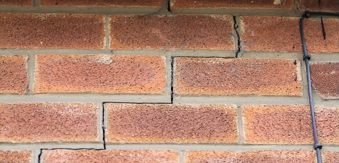 crack runs through mortar of brick wall, indicating foundation damage