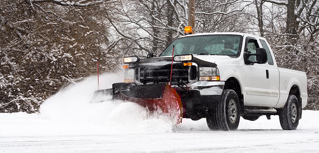 pickup truck with plow attached pushes snow off road