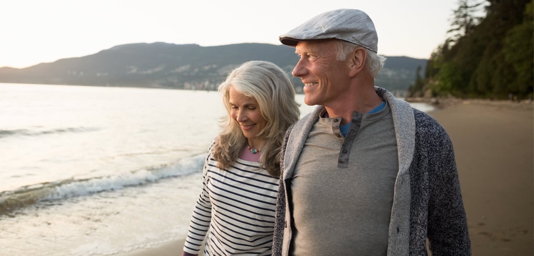 senior man and woman walk together on the beach