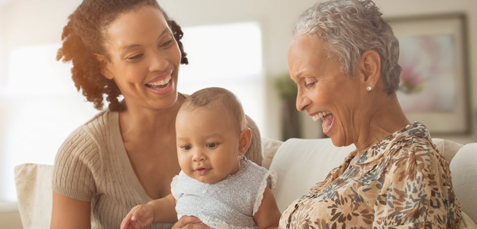 mother, baby, and grandmother sit and smile on couch