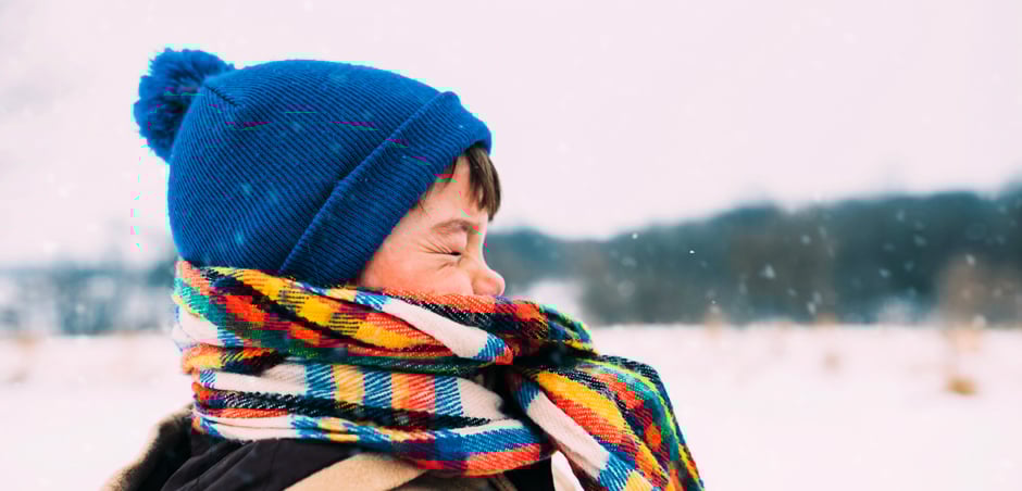 young boy wears scarf and hat on snowy day