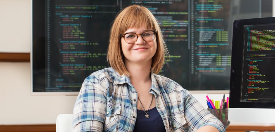 woman smiles in front of computer monitors in office setting