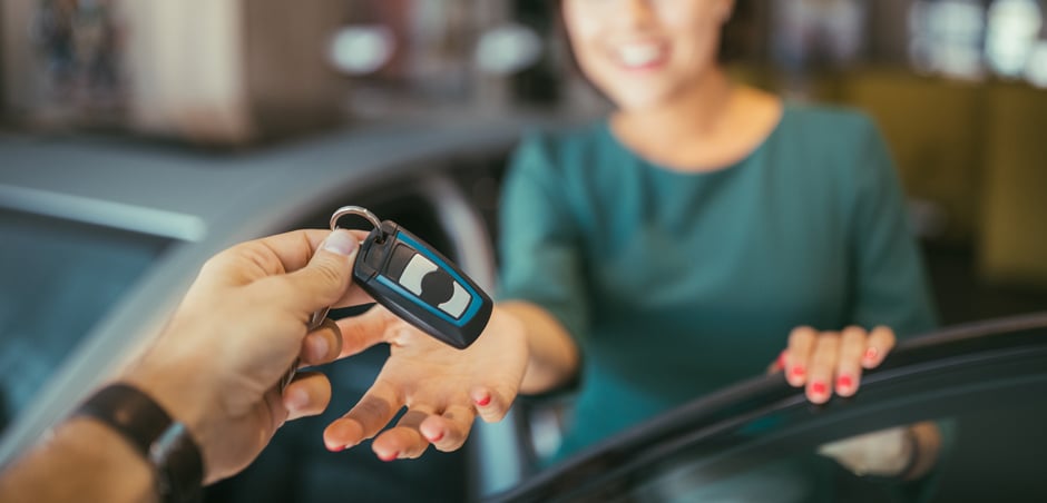 woman standing outside car receives car keys from person out of frame