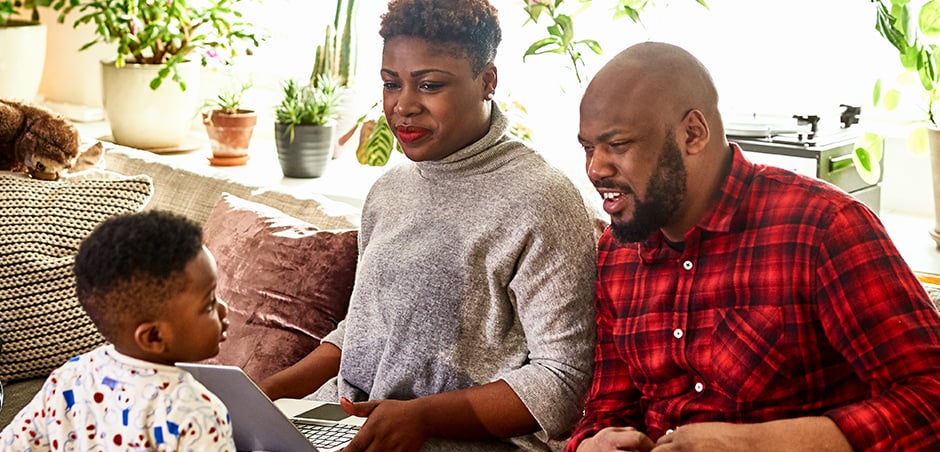 woman and man sit on couch with laptop while small child looks on