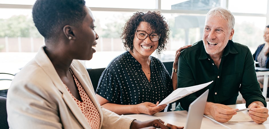 smiling, professionally dressed couple meets business woman to review papers