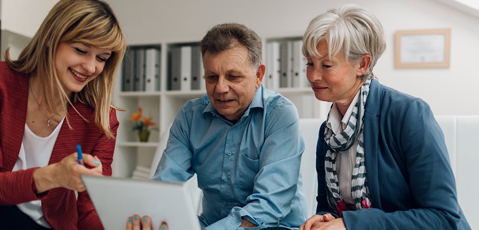 professionally dressed woman reviews document with older, casually dressed man and woman