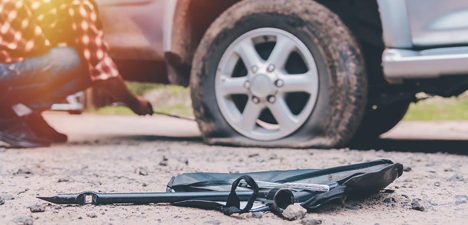 medium shot of flat tire on a car; equipment in the foreground and person kneeling next to tire in background