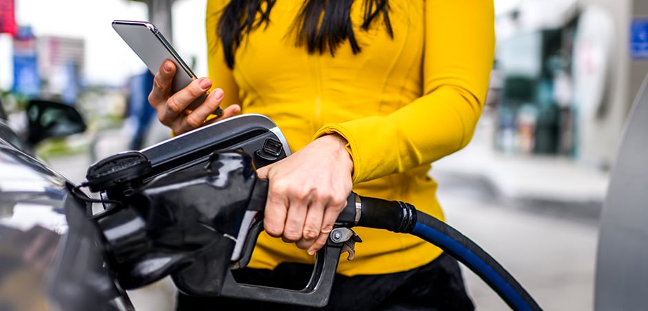 woman fills up her tank with gas while holding smartphone in hand