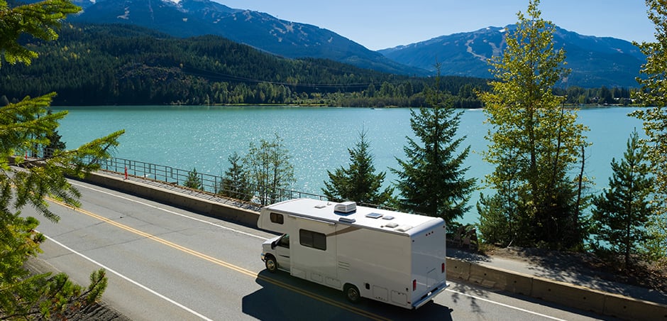 aerial view of RV driving alongside scenic alpine lake