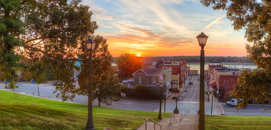 wide shot of a small town at sunset, with grassy park in foreground and brick buildings in background