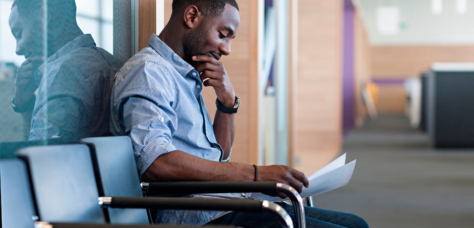 man sits at the end of a row of chairs, thoughtfully holding his chin and reading papers