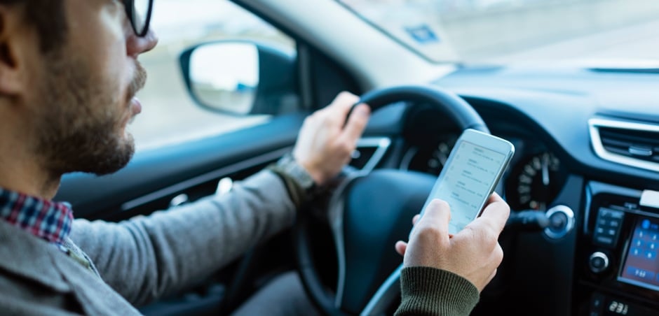 man drives car while holding smartphone in right hand by steering wheel
