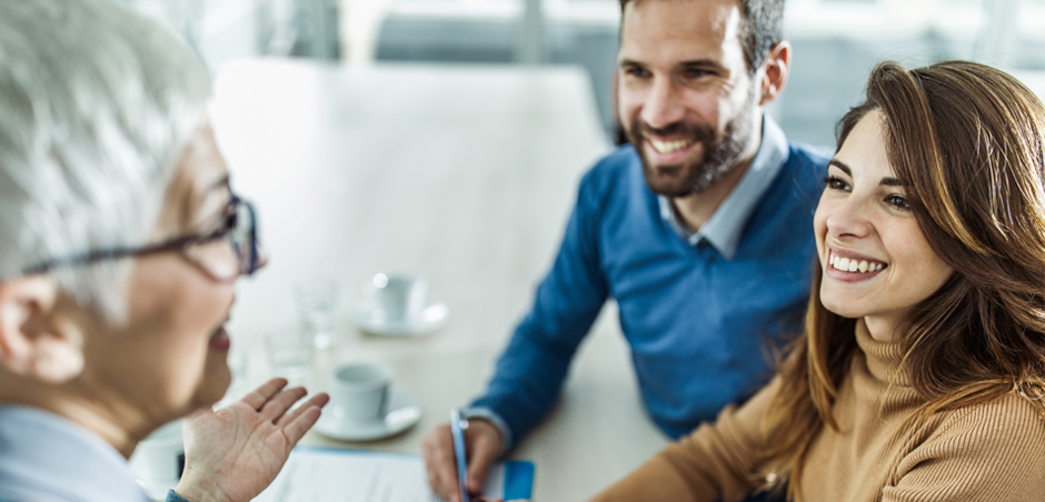 Man and woman meet with silver haired professional at conference table