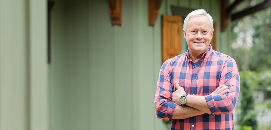 man standing in front of a green house with folded arms