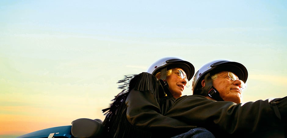 A man and woman ride a motorcycle with the sunset in the background.