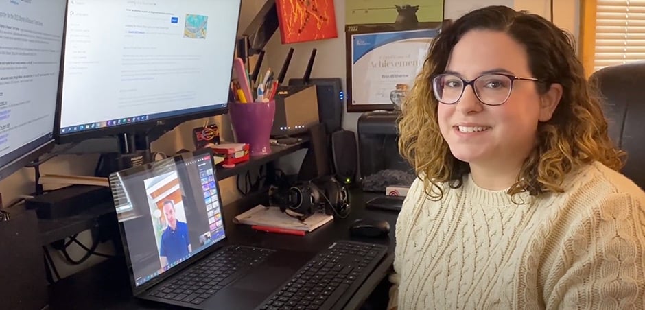 a woman with glasses and a white sweater sits to the right of her desk