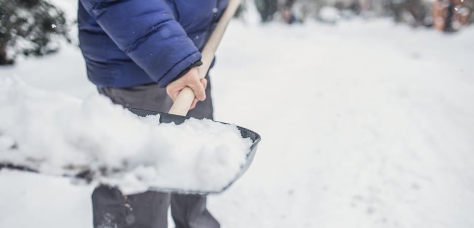 A person in a puffy winter jacket tosses a shovel full of snow.