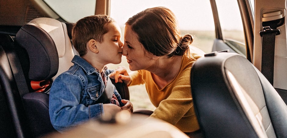 a woman buckling a little boy into his carseat in the back seat of the car