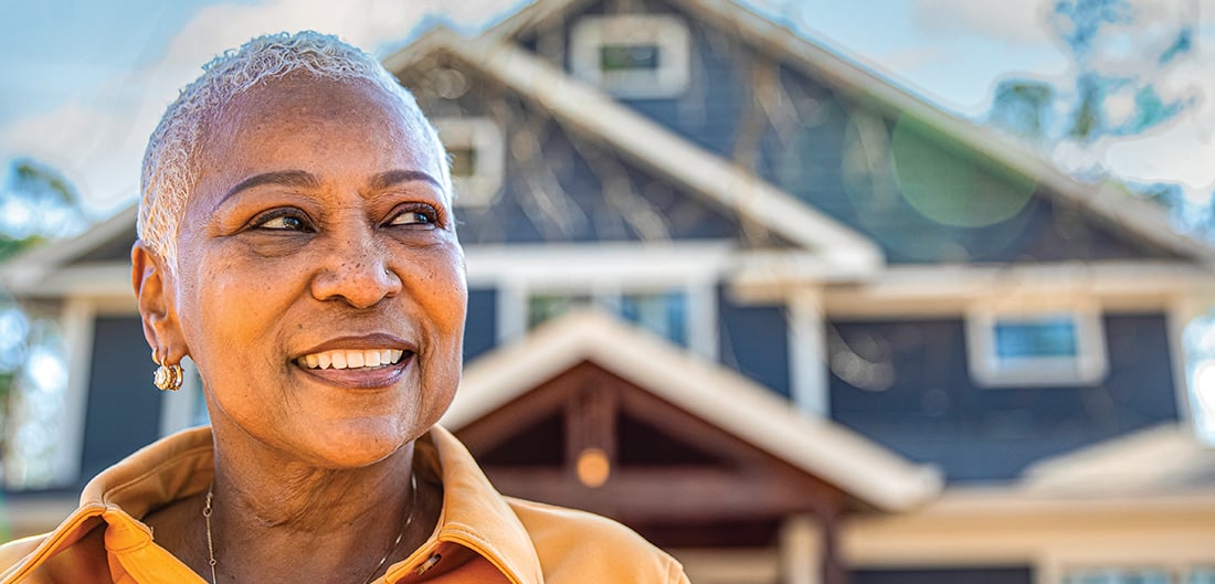 Older woman smiling in front of a house.