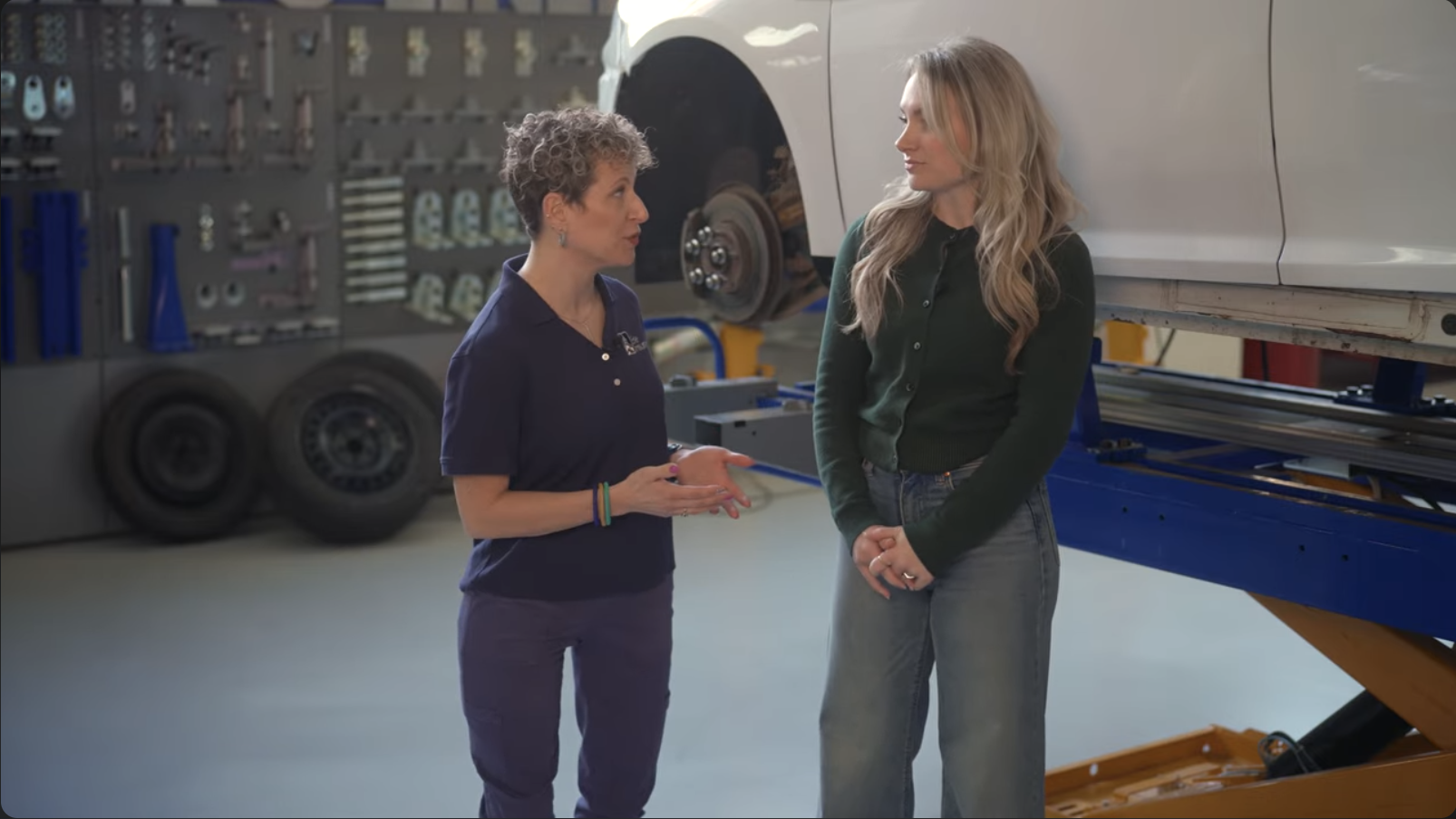 two women standing in front of a car on a lift