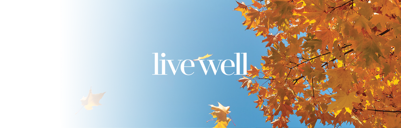 Looking up at the sky through a tree with Fall leaves and the words live well