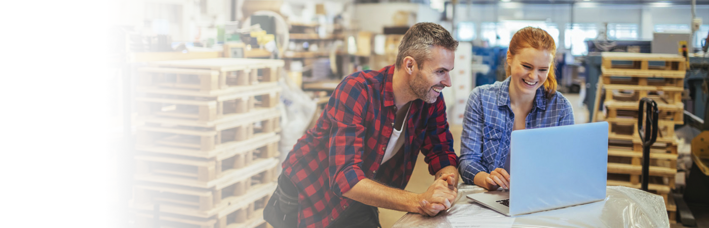 People smiling at laptop while surrounded by stacks of pallets