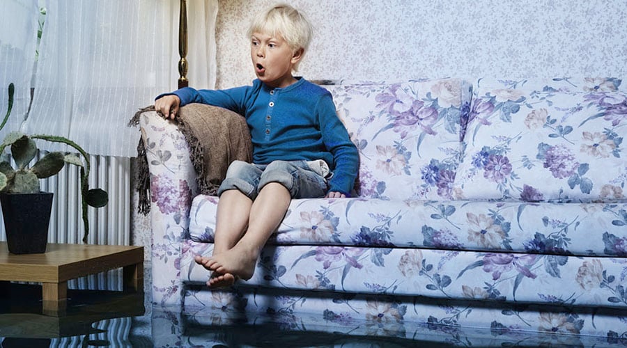 Boy sitting on couch in flooded room